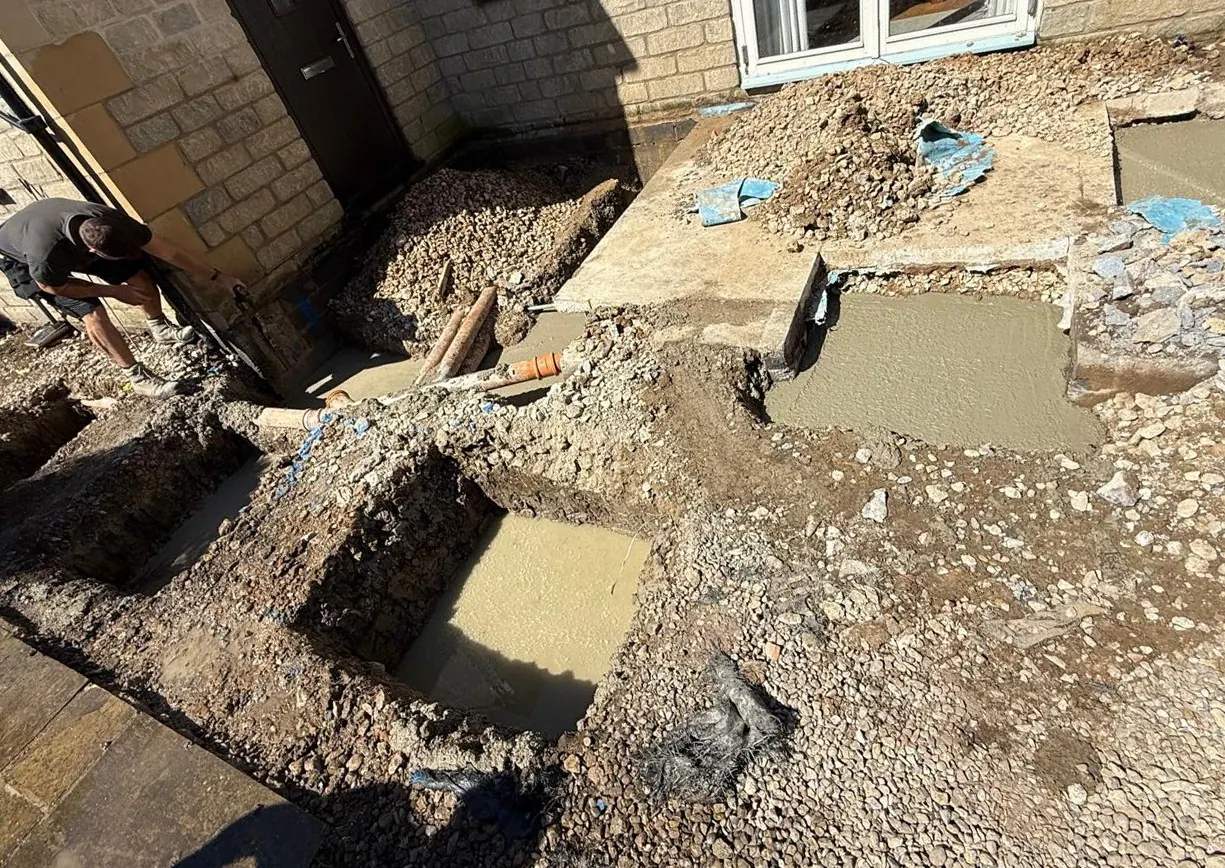 Concrete foundations and new drainage pipes being laid in trenches beside a stone house