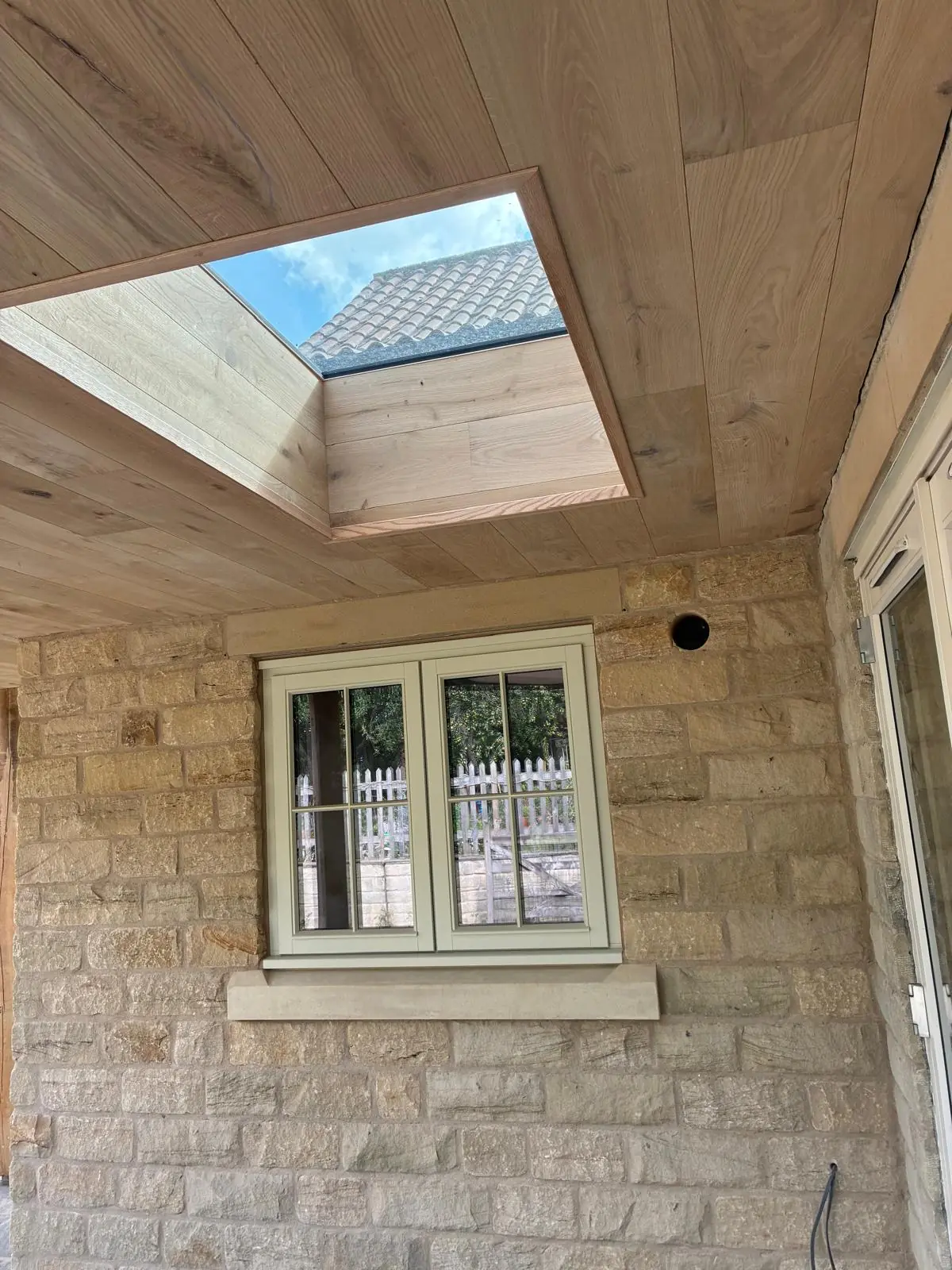 Oak-lined canopy soffit with a framed roof light above a stone wall and painted timber window