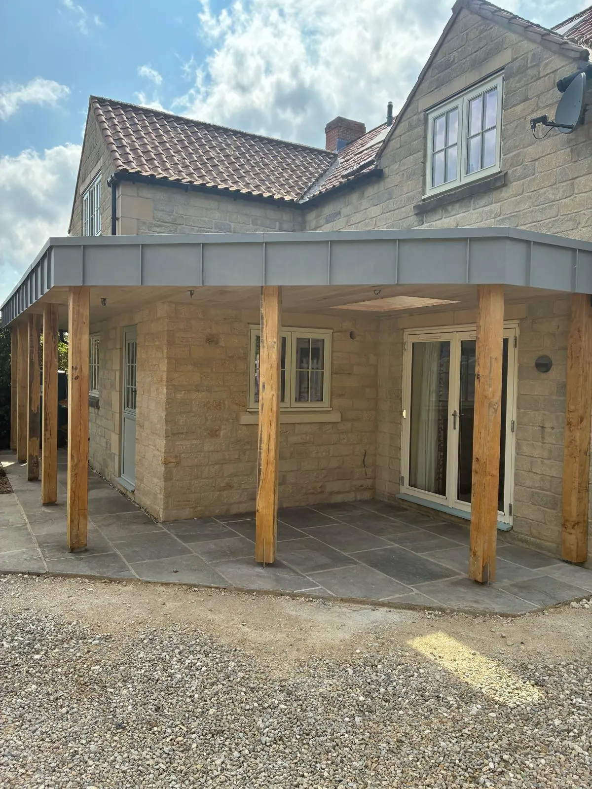 Flat-roofed rear canopy with an aluminium fascia, oak posts and a stone-flagged terrace